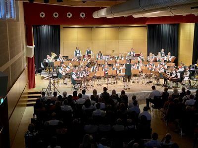 Eine Band spielt auf der Bühne mit verschiedenen Musikinstrumenten vor einem Publikum in einem Saal.