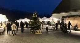 Bei Nacht versammeln sich Menschen um einen Weihnachtsbaum auf einem Freiluftmarkt mit Zelten und Dekorationen.