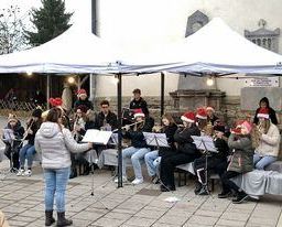 Eine Gruppe von Musikern mit Weihnachtsmützen spielt unter einem weißen Zelt, mit einem Dirigenten vor ihnen und Instrumenten auf dem Tisch.