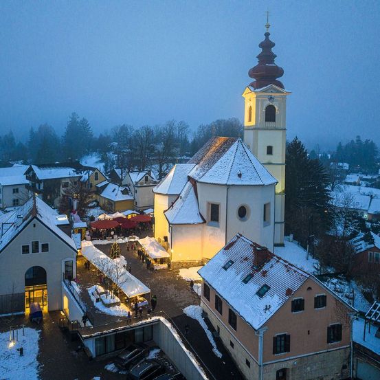 Ein Luftbild einer kleinen Stadt mit einer Kirche in der Mitte. Die Stadt ist schneebedeckt. Es gibt mehrere Häuser und Gebäude in der Gegend.