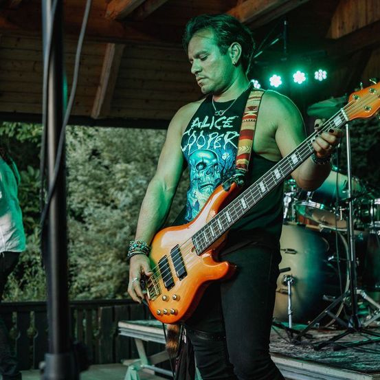 Ein Mann spielt auf der Bühne mit einer E-Gitarre. Er trägt ein ärmelloses Shirt mit dem Schriftzug Alice Cooper.