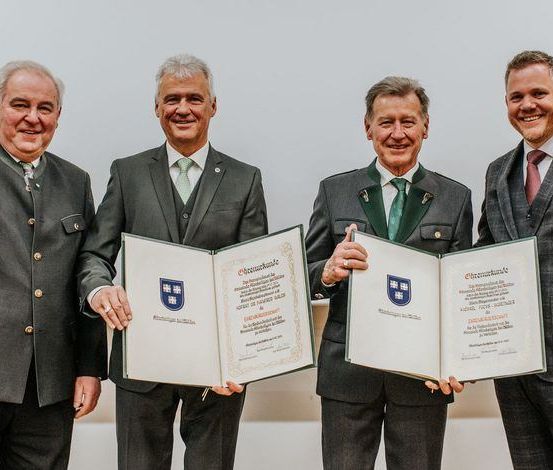 Vier Männer in Anzügen lächeln und halten Urkunden mit einem Universitätslogo in den Händen, möglicherweise zur Feier einer Errungenschaft.
