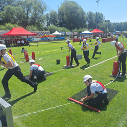 Eine Gruppe von Personen in Schutzausrüstung führt auf einem Feld eine Feuerwehrübung durch, wobei einige laufen und andere Feuerlöscher handhaben.