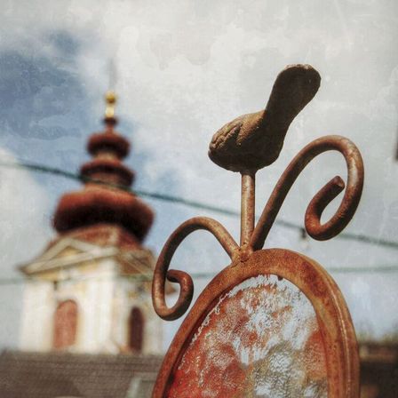 Nahaufnahme eines rostigen Metallschilds mit einem Vogel auf der Spitze, verwaschener Hintergrund eines historischen Gebäudes mit einer Kuppel.