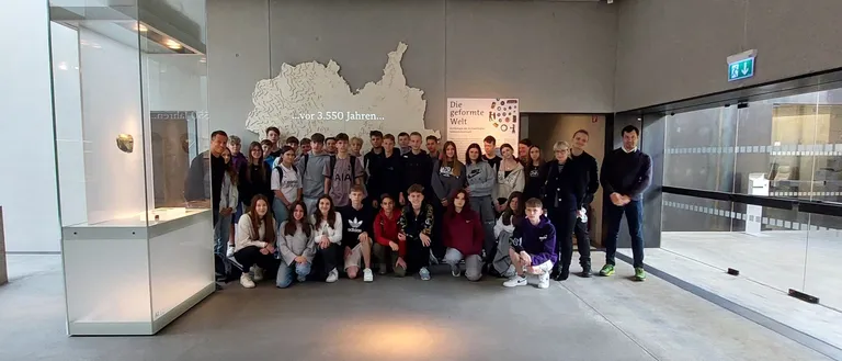 Eine Gruppe von Menschen posiert für ein Foto in einem Museum. Ein Kartenausschnitt von Deutschland ist im Hintergrund sichtbar.