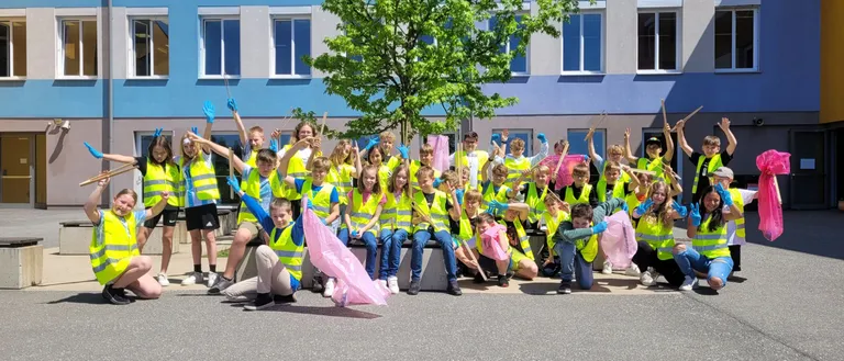 Eine Gruppe junger Menschen in gelben Westen und Handschuhen posiert für ein Foto vor einem Gebäude mit blau-weißen Fenstern.