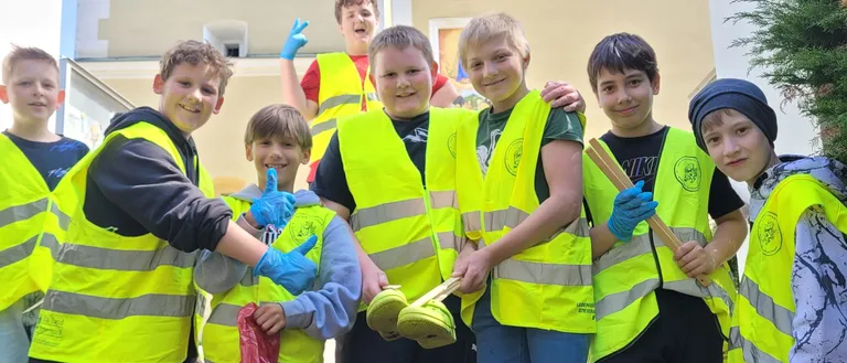 Eine Gruppe junger Jungen in reflektierenden Westen und Handschuhen, lächelnd und mit Stöcken, stehen auf Stufen mit Müllsäcken.