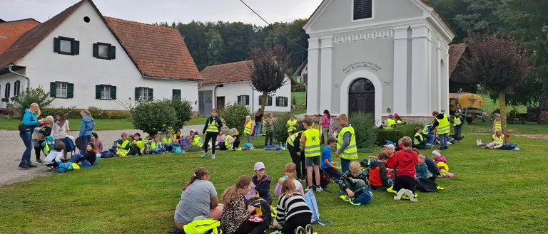 Eine Gruppe von Kindern und Erwachsenen sitzt auf dem Rasen vor einer Kirche.
