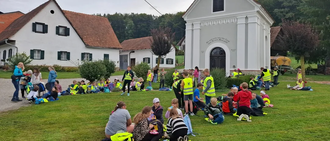 Eine Gruppe von Kindern und Erwachsenen sitzt auf dem Rasen vor einer Kirche.