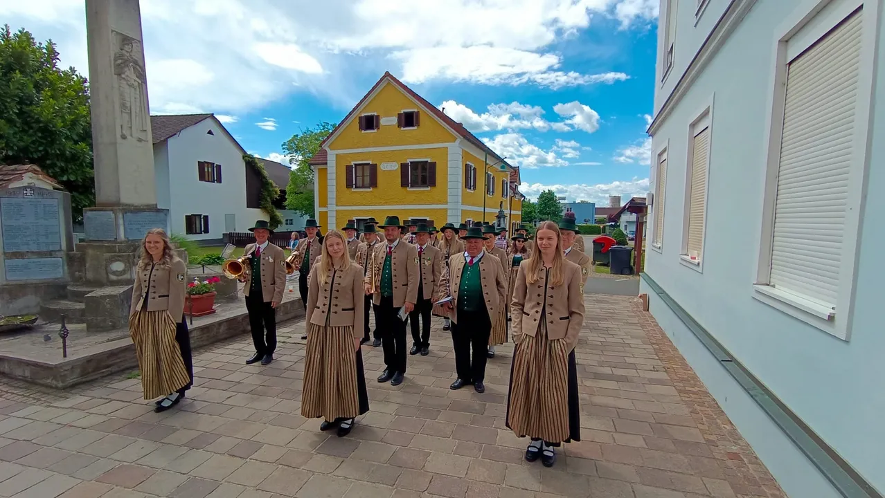Eine Gruppe von Musikern in traditioneller Kleidung posiert für ein Foto vor einem gelben Haus unter einem blauen Himmel mit Wolken.