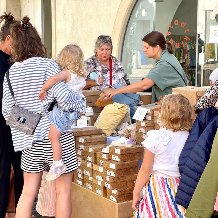 Eine Gruppe von Frauen und Kindern versammelt sich um einen Tisch mit Schuhkartons. Eine Frau in einem grünen Shirt hält einen Schuh und zeigt ihn einem Kind.