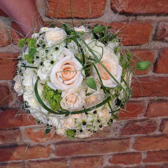 Ein Nahaufnahme einer weißen Rosenbouquet mit grünen Blättern und einer Ziegelmauer im Hintergrund.