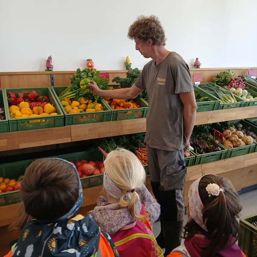 Ein Mann unterrichtet eine Gruppe von Kindern über Gemüse in einem Supermarkt.
