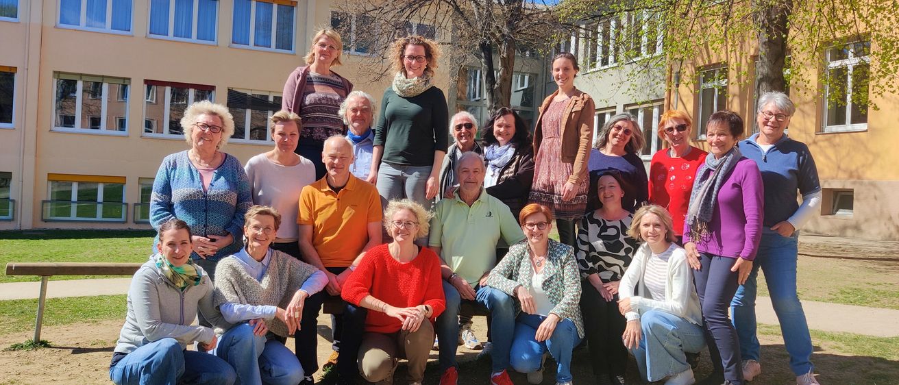 Eine Gruppe von Menschen posiert für ein Foto vor einem Gebäude mit Bäumen und Gras im Vordergrund.