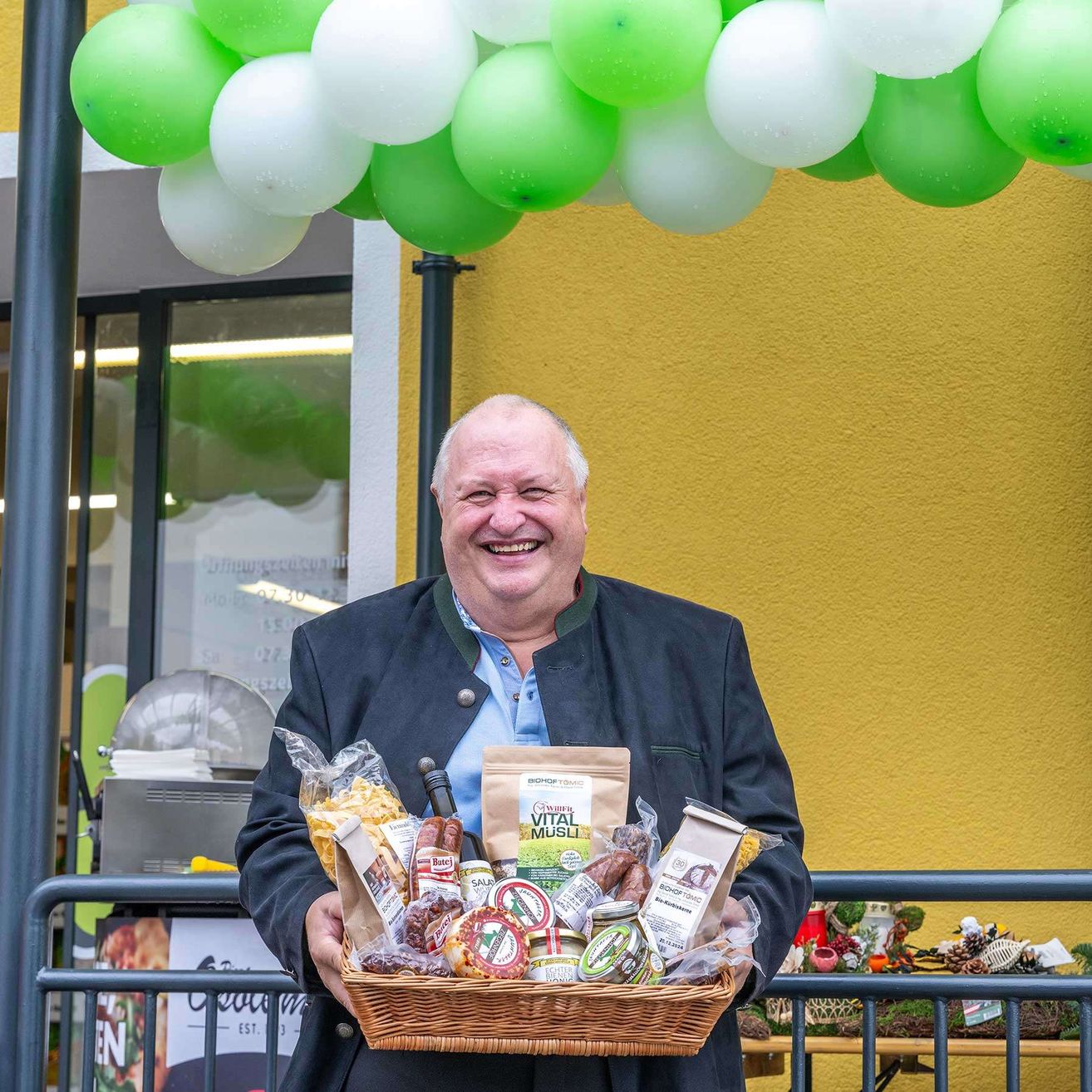 Ein Mann, der einen Korb mit Essen und Getränken vor einem Geschäft hält, mit Luftballons über ihm.