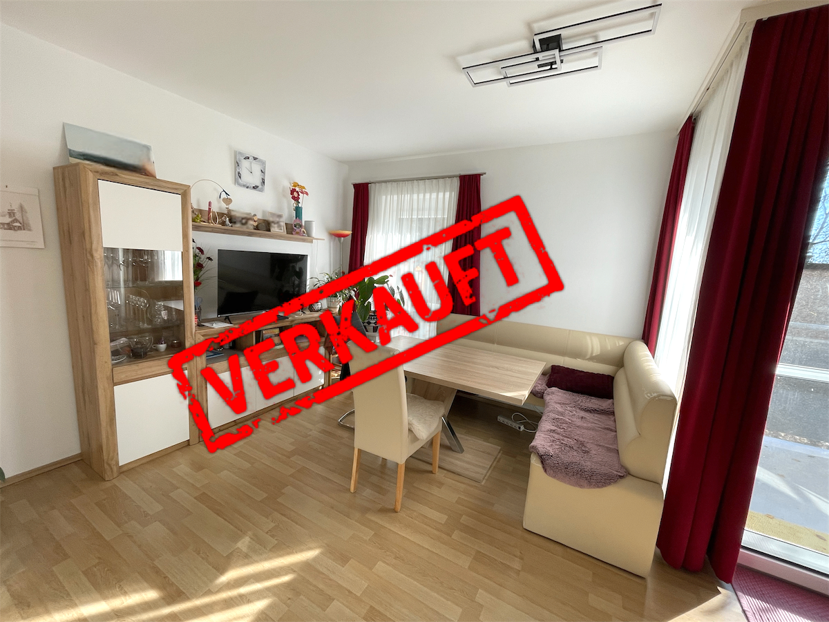 Ein leeres Wohnzimmer mit Esstisch, Sofa und Fernseher. Das Wort 'Verkauft' ist in Rot geschrieben.