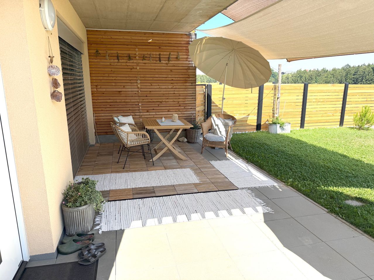 Eine Holzterrasse mit Tisch, Stühlen und einem Regenschirm. Die Terrasse hat einen Holzboden, eine Holzwand und einen Rasenbereich.