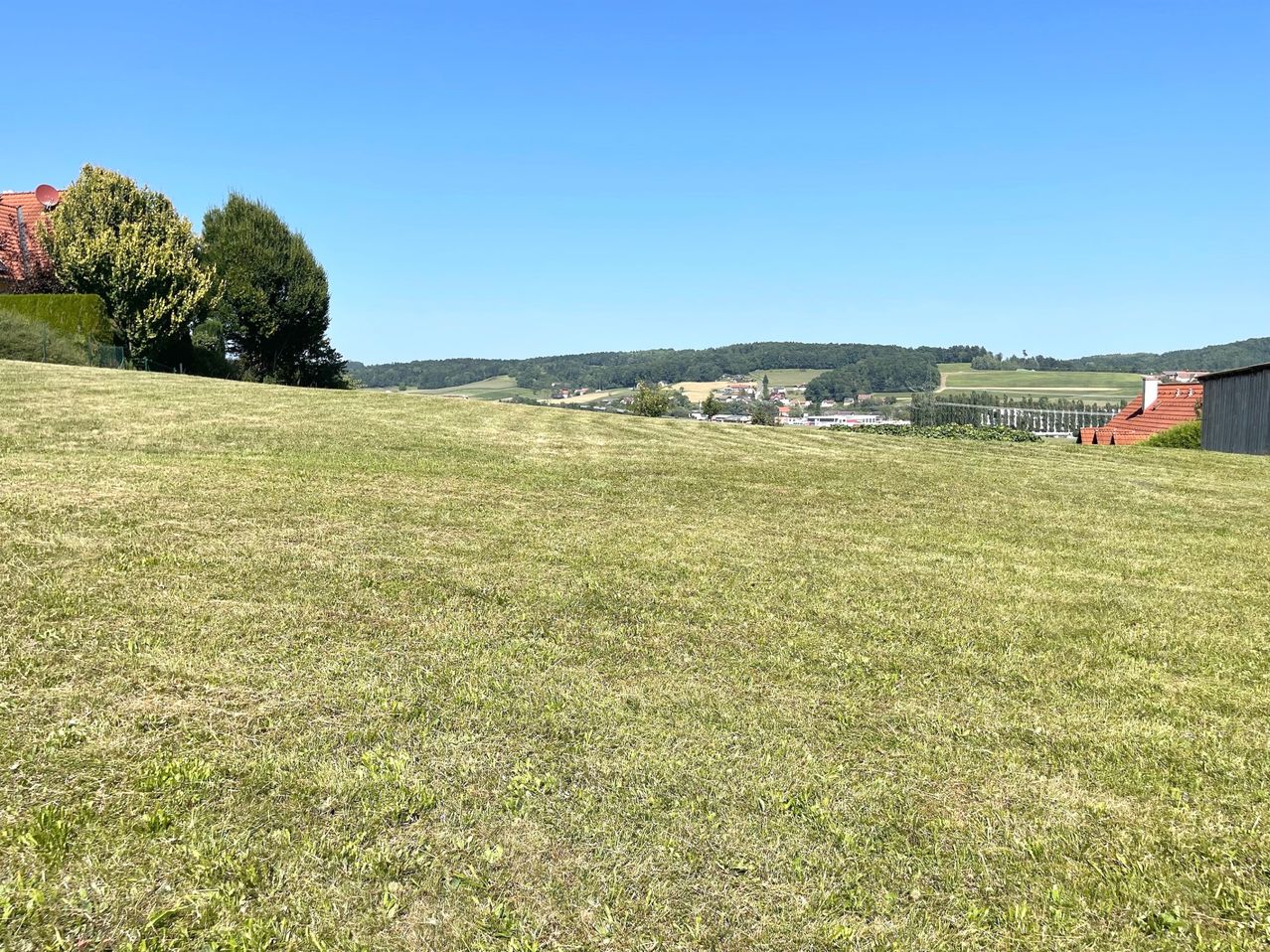 Ein weitläufiges, offenes Grasfeld unter einem klaren blauen Himmel mit entfernten Hügeln und einer kleinen Stadt.