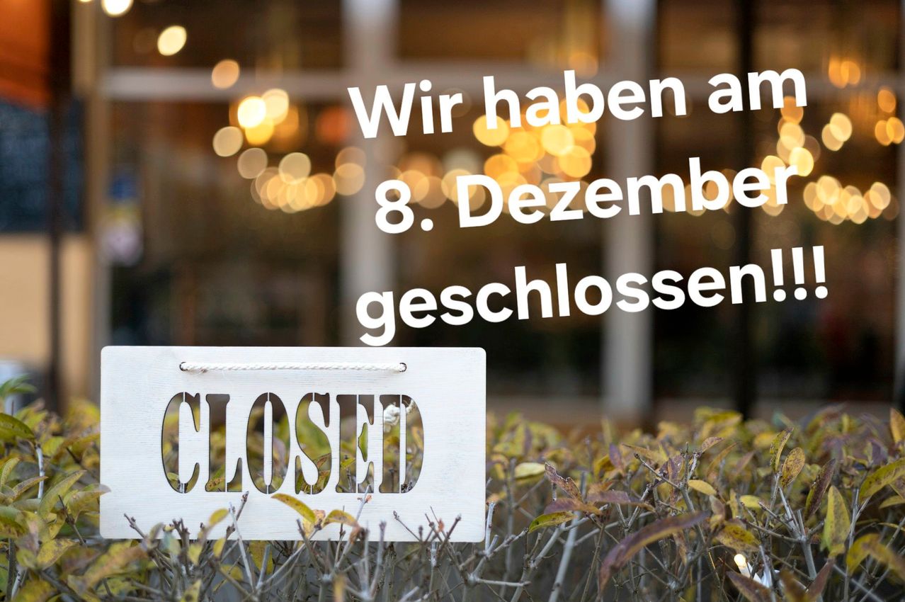 Ein geschlossenes Schild an einem Schaufenster zeigt in großen Buchstaben 'CLOSED'. Dahinter zeigt ein verschwommener Hintergrund ein Gebäude mit Bokeh-Lichtern. Über dem Schild steht in deutscher Sprache 'Wir haben am 8. Dezember geschlossen'.
