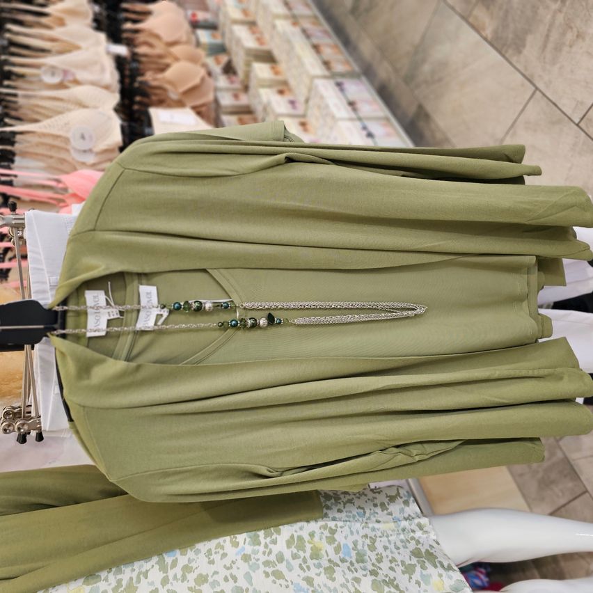 Ein grünes Blusenkleid mit Falten und eine Halskette mit Perlen werden in einem Bekleidungsgeschäft ausgestellt.