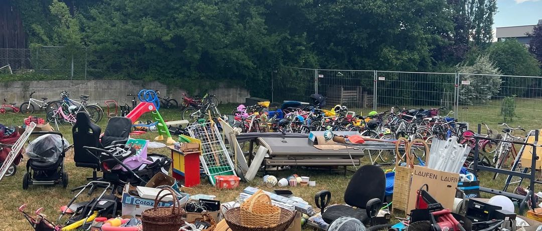 Ein Flohmarkt mit verschiedenen Artikeln, darunter Fahrräder, Spielzeug und Haushaltsgegenstände, an einem sonnigen Tag.