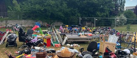 Ein Flohmarkt mit verschiedenen Artikeln, darunter Fahrräder, Spielzeug und Haushaltsgegenstände, an einem sonnigen Tag.