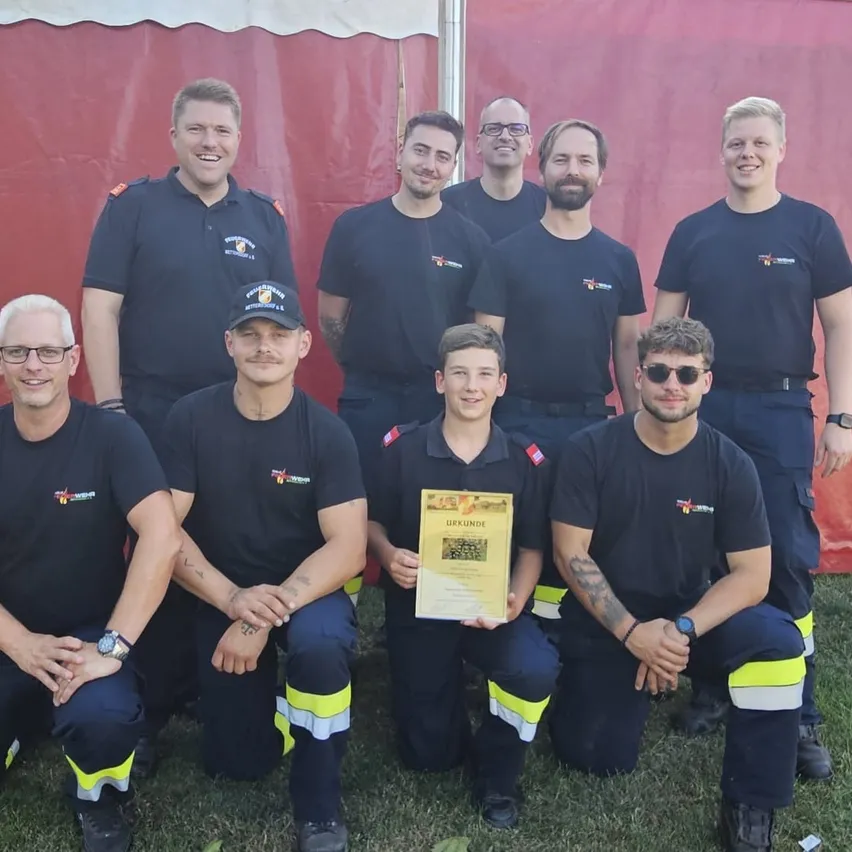 Eine Gruppe von Feuerwehrleuten in Uniform posiert für ein Foto mit einem jungen Jungen, der ein Zertifikat in der Hand hält.