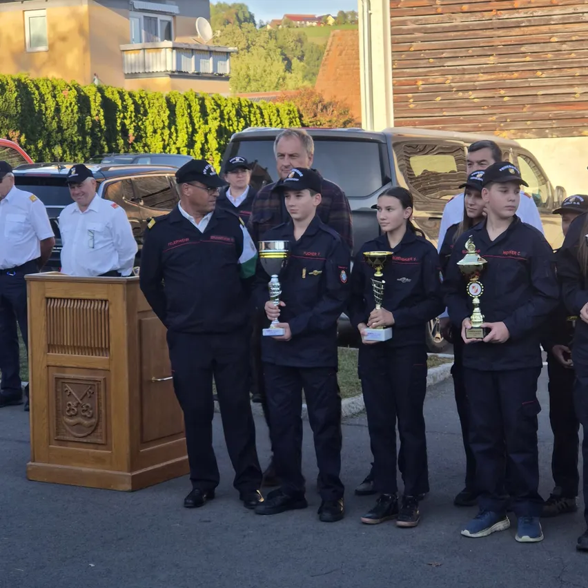 Eine Gruppe junger Menschen in Uniform steht mit Trophäen bei einer Zeremonie, mit Beamten und Zuschauern im Hintergrund.