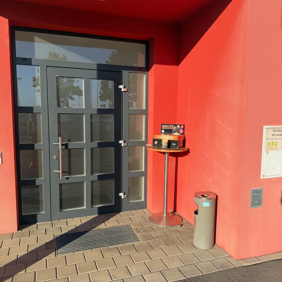 Ein rotes Gebäude mit einer Glastür und einem kleinen Tisch mit einer Schachtel darauf.