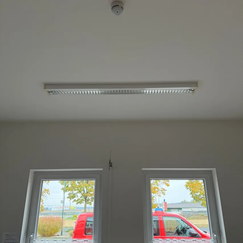 Ein Raum mit zwei Fenstern, einer weißen Decke und einem roten Auto, das durch die Fenster zu sehen ist.