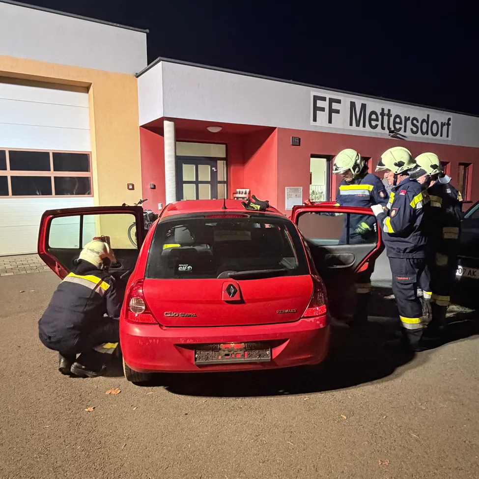 Eine Gruppe von Feuerwehrleuten arbeitet an einem roten Renault Clio Auto vor einem Feuerwehrhaus in der Nacht.