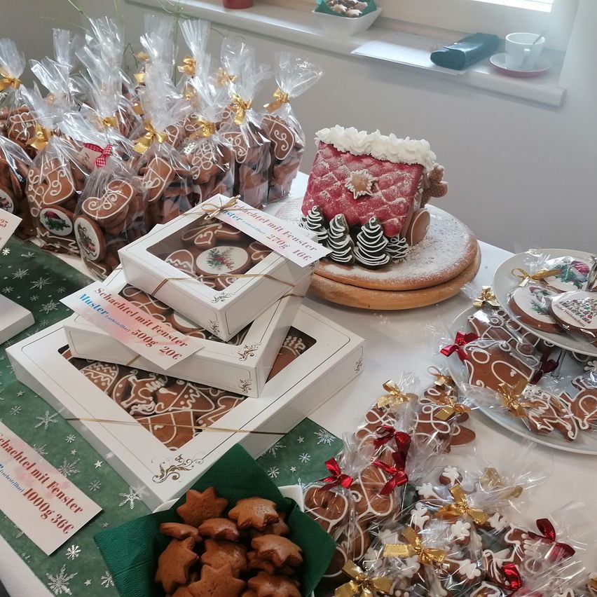 A table filled with various gingerbread cookies in boxes and bags. There are several boxes of gingerbread, some individually wrapped, and a gingerbread house with a snowy roof.