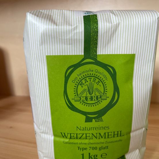 Ein Beutel mit 1 kg glattem Weizenmehl, gekennzeichnet mit 'Naturreines Weizenmehl', Typ 700, ohne chemische Zusatzstoffe, auf einer Holzoberfläche.