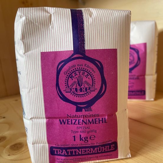 Ein Sack 'Trattnemermuhle' Weizenmehl, 1 kg, Typ 480, von einer natürlichen Getreidemühle, garantiert ohne chemische Zusatzstoffe, mit einem violetten Etikett auf einer Holzoberfläche.