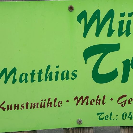 Ein grünes Schild mit weißem Text lautet 'Muthius Cre'. Darunter stehen die Worte 'Kunstmühle Mehl Ge' und eine Telefonnummer 'Tel.: 04'.