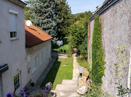 Ein Hinterhof mit einem Rasenbereich, einem Basketballkorb und einem Haus mit rotem Dach.