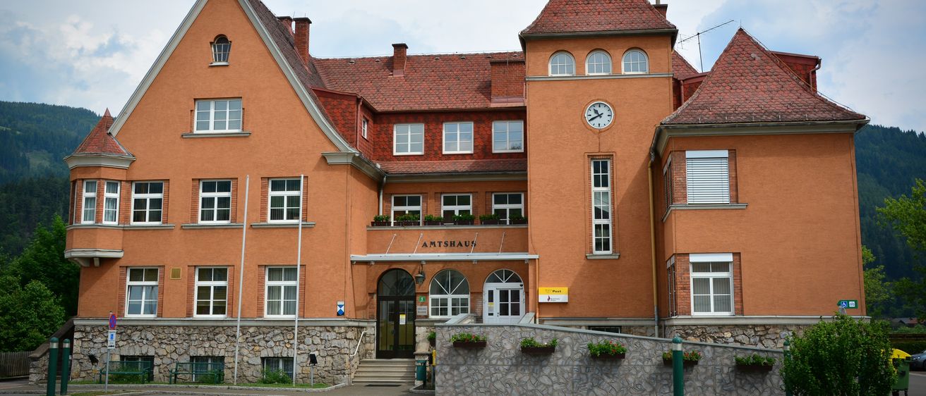 Das Amtshaus-Gebäude mit einer Uhr an der Wand und Pflanzen auf dem Zaun draußen.