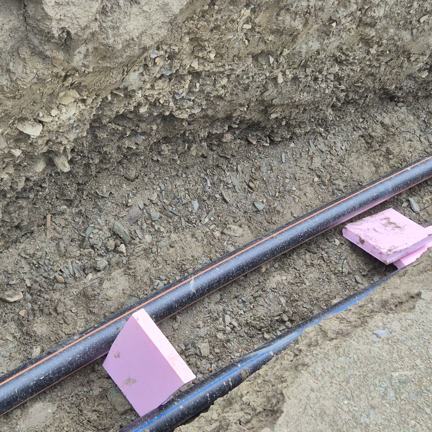 Ein schwarzer Rohr ist mit zwei rosa Schaumstoffblöcken im Boden vergraben. Der Boden scheint trocken zu sein und hat kleine Steine.