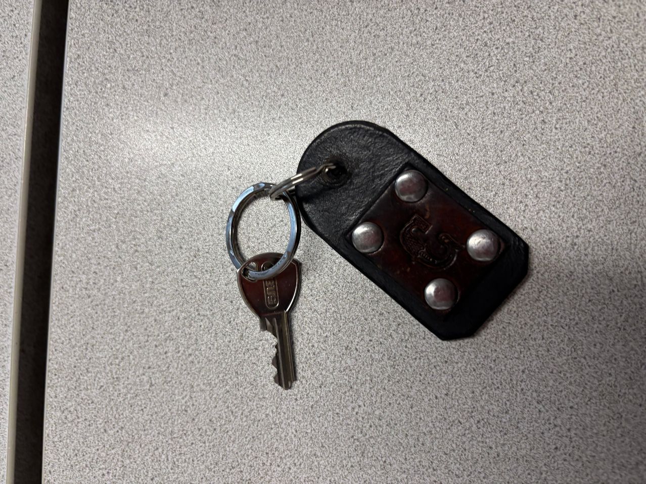 Ein Schlüssel mit einem Metallring ist an einem schwarzen Lederschlüsselanhänger auf einer grauen Oberfläche befestigt.
