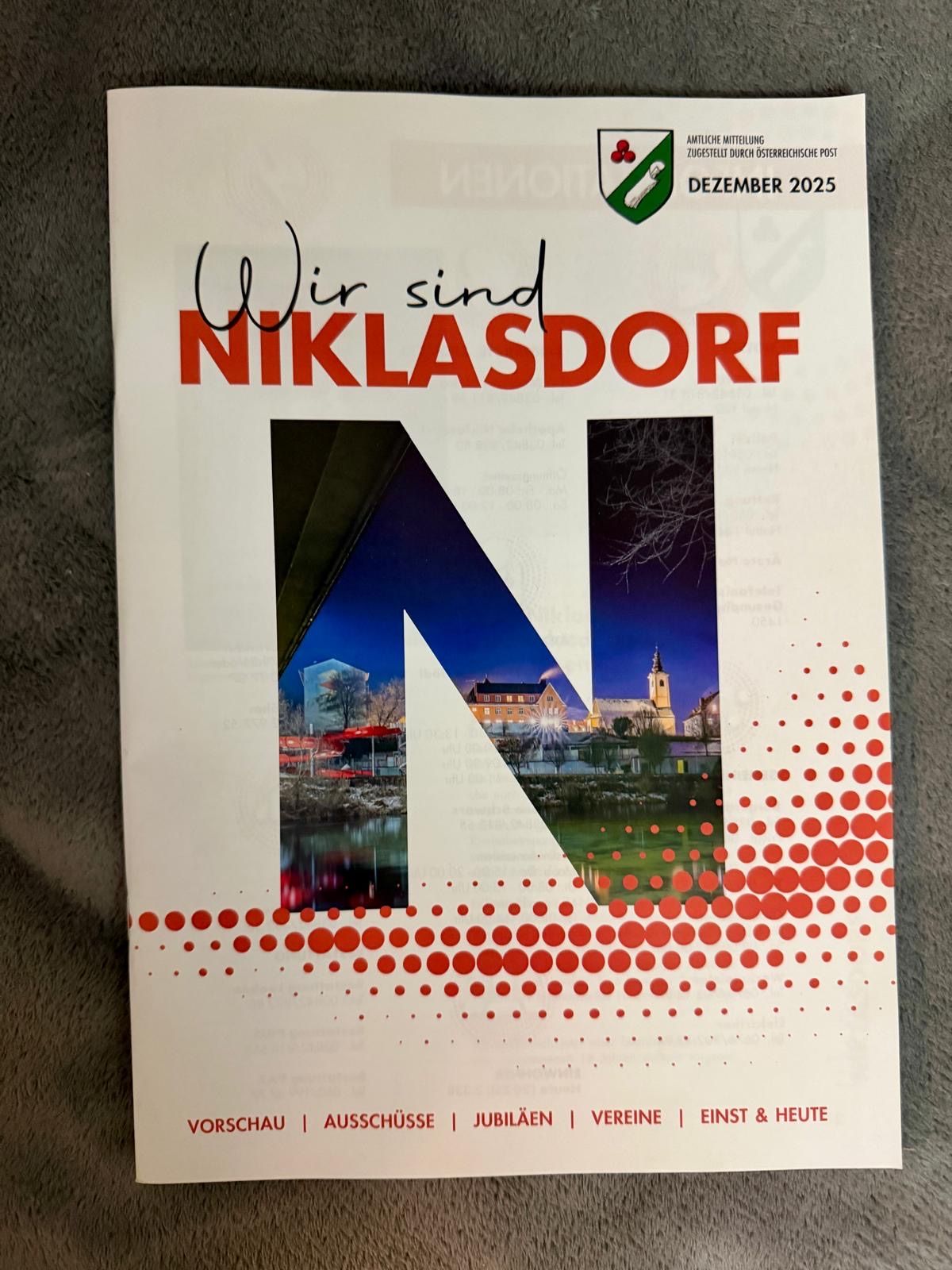Die Titelseite eines Heftes mit dem Titel 'Wir sind Niklasdorf' vom Dezember 2025. Es zeigt eine Collage von Bildern, darunter ein Gebäude, eine Straße und einen Stadtplatz. Der Einband hat einen roten Rand mit Punkten.