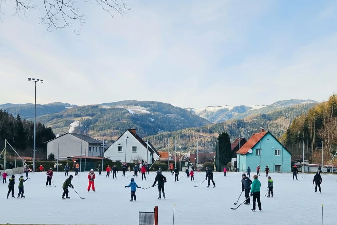 Eishockey im Freien auf einem gefrorenen Teich mit Menschen in warmer Kleidung und schneebedeckten Bergen im Hintergrund.