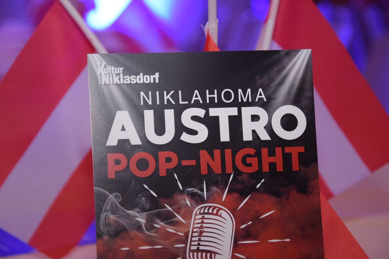 Ein Werbebanner für die Austro Pop-Nacht in Niklasdorf Kultur, mit einem Mikrofon und rauchartigen Effekten in Rot und Schwarz.