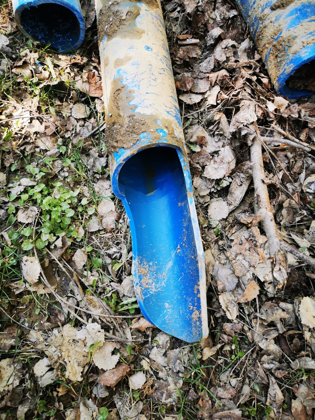 Eine zerbrochene blaue Röhre liegt auf dem Boden, bedeckt mit trockenen Blättern und Schlamm.