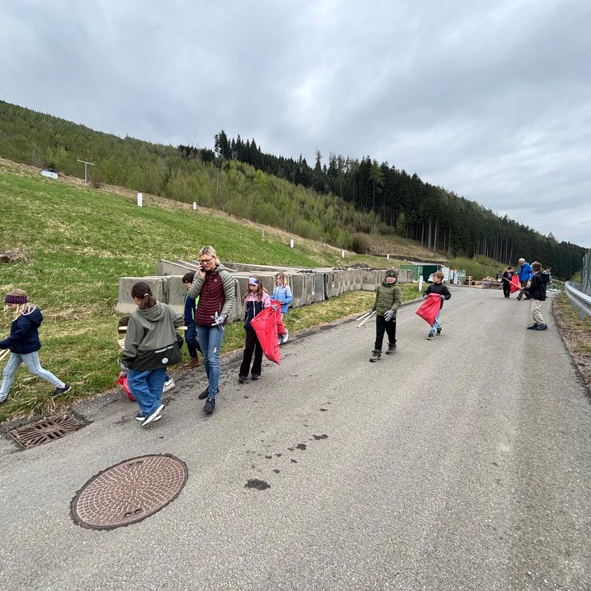 Eine Gruppe von Menschen, einige mit roten Taschen, geht einen Weg entlang, der an einer Seite einen Hang hat. Eine Person in der Mitte hält ein Telefon.