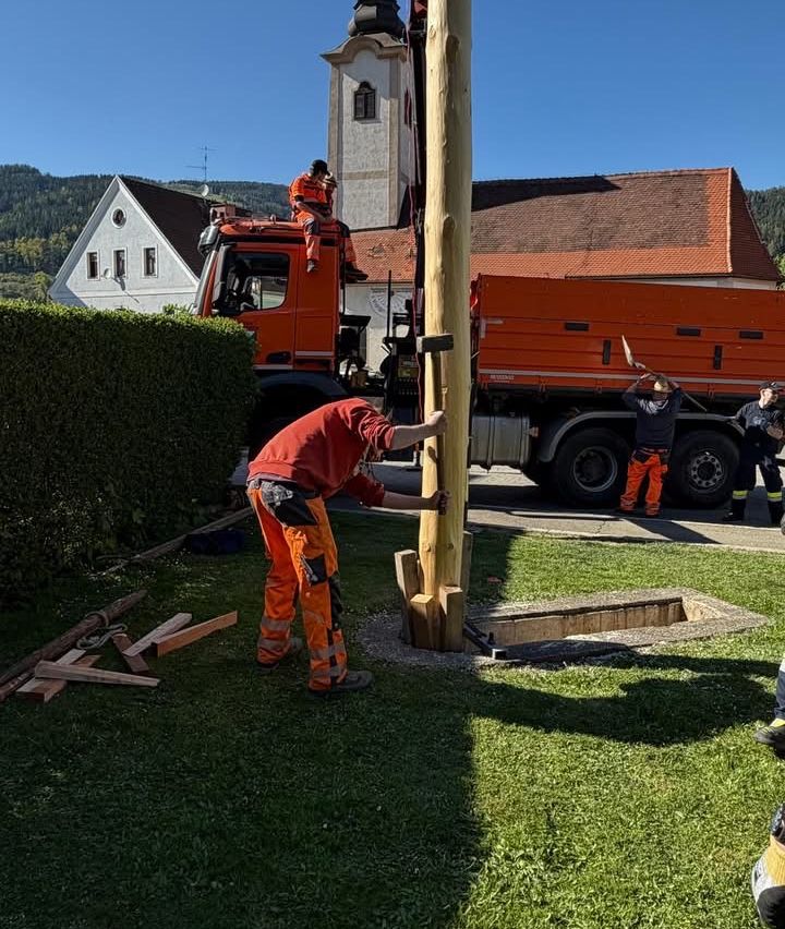 Eine Gruppe von Arbeitern installiert einen Holzpfahl vor einem Gebäude, mit einem geparkten Lastwagen in der Nähe.
