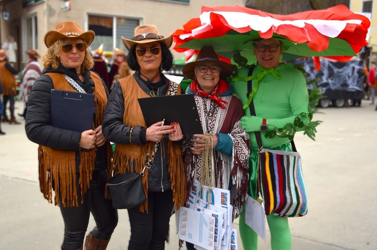 Vier Menschen in Kostümen posieren für ein Foto. Zwei Frauen tragen Cowboyhüte und Westen. Die Frau in der Mitte hält eine Mappe. Ein Mann in Grün trägt ein Blattkostüm.