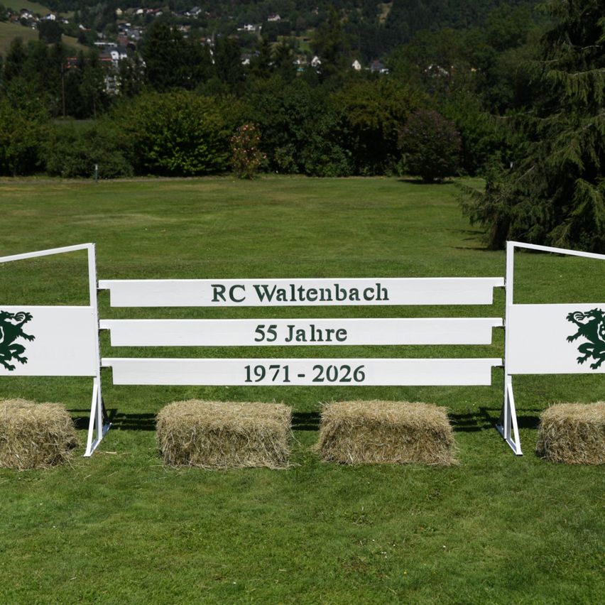 A white banner with the text 'RC Waltenbach 55 Jahre 1971-2026' and green lion logos on a grassy field with hay bales.