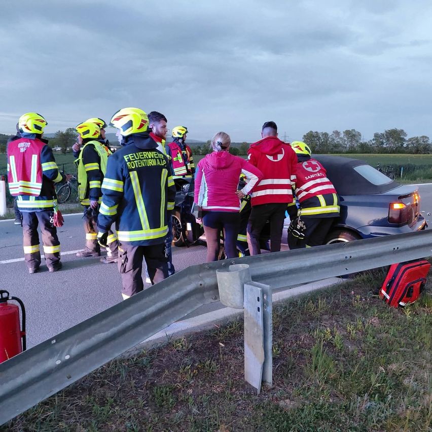 Emergency responders are attending to a car accident. Firefighters and paramedics are present, with one individual receiving medical assistance.