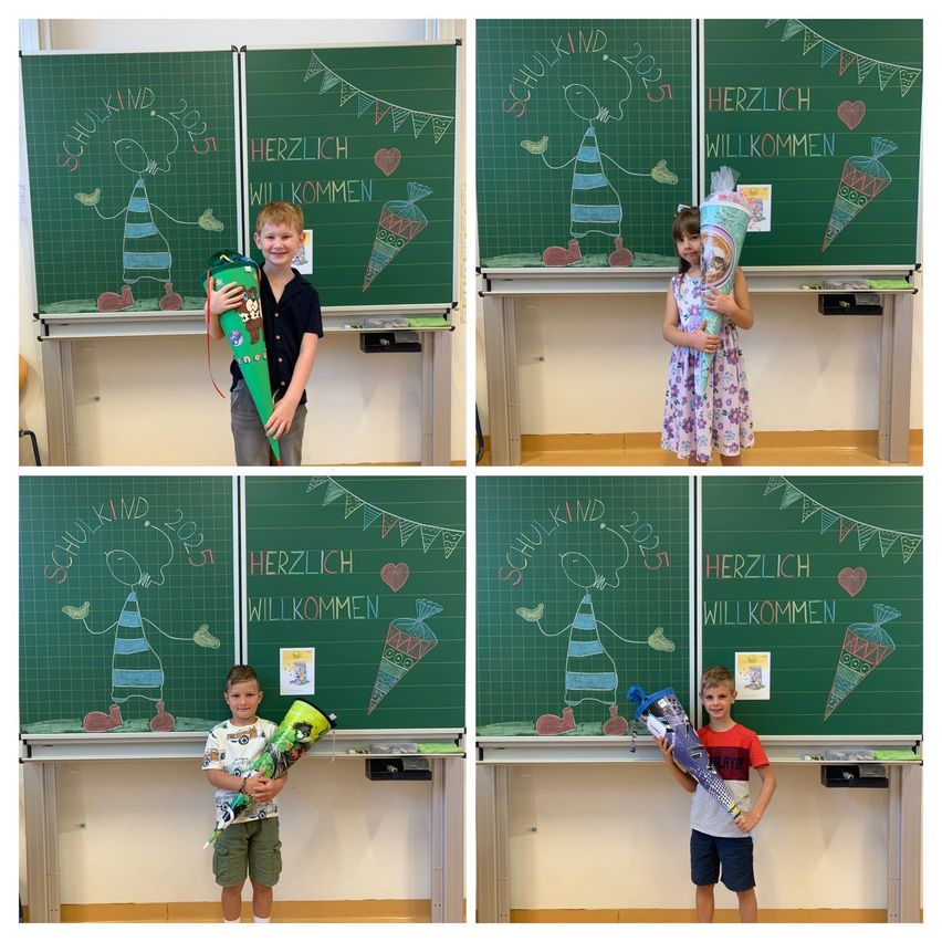 Vier Kinder stehen vor grünen Tafeln mit Zeichnungen und Botschaften. Jedes Kind hält einen Blumenstrauß. Die Botschaften auf den Tafeln lauten 'SCHULKIND 2023' und 'HERZLICH WILLKOMMEN'.