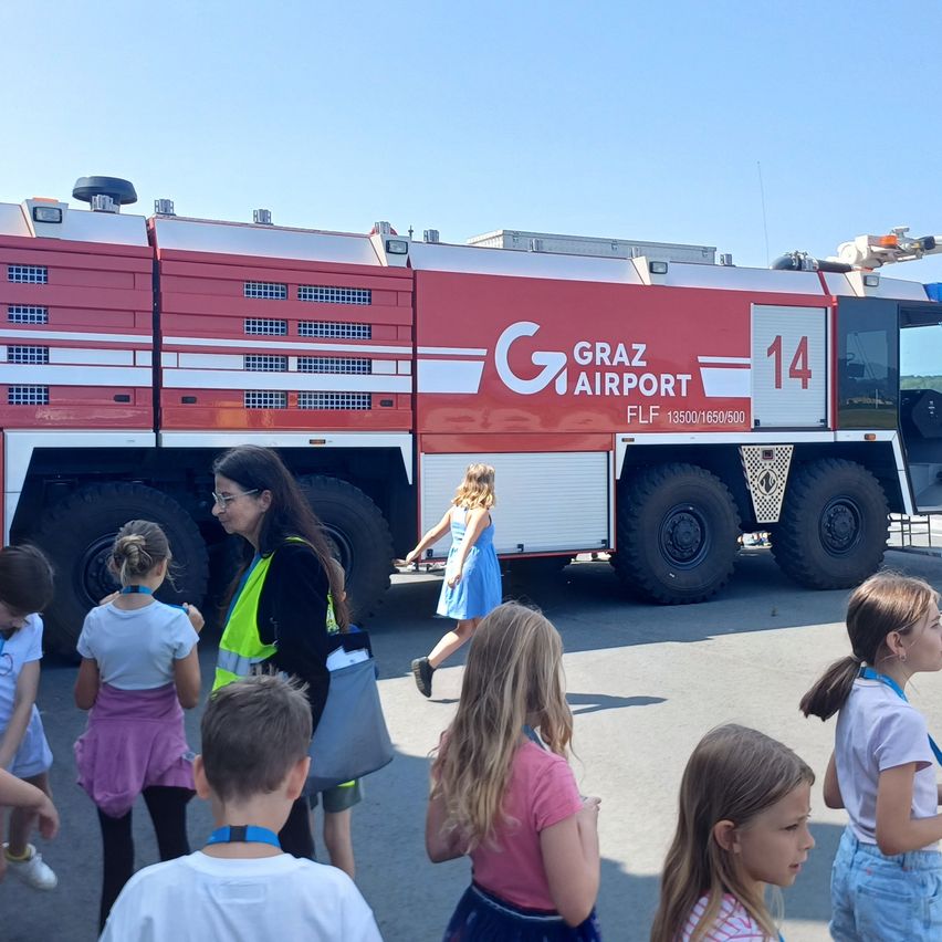 Eine Gruppe von Kindern steht vor einem roten Graz Airport Feuerwehrauto mit der Nummer 14 auf der Seite.